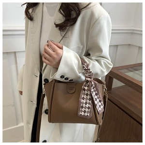 Détail du sac à main marron foncé en cuir grainé avec foulard décoratif et logo métallique