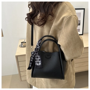 Détail du sac seau en cuir grainé noir avec foulard décoratif et logo gravé dessus