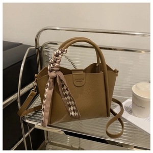 Détail du sac seau marron avec texture litchi et foulard en soie élégant sur la poignée
