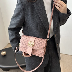 Pink minimalist crossbody bag with letter M print and gold buckle on a gray blazer model