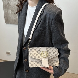 Sac sous le bras beige chic avec imprimé monogramme M et boucle dorée porté par un mannequin