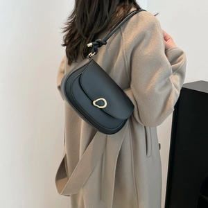 Chic black leather saddle shoulder bag with golden buckle on a camel coat model