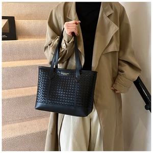 Detail of black woven texture tote bag featuring a gold metal brand logo for daily fashion