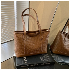Detail of dark brown woven leather tote bag with Intrecciato texture on art books