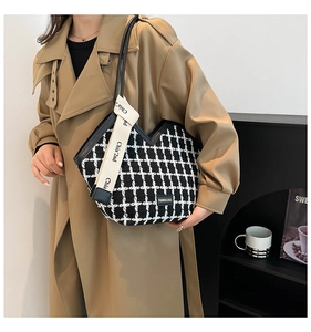 Detail of black and white plaid tweed tote bag with wide beige lettered strap and leather patch