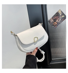 Detail of white saddle bag featuring a knotted strap and gold geometric buckle
