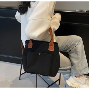 Vue détaillée du sac cabas en toile noire avec anses brunes et bouton-pression argenté