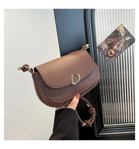 Detail of a brown leather crescent saddle bag with a unique gold knot strap and metallic clasp