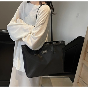 Detailed view of black waterproof nylon tote bag with leather logo patch and slim straps