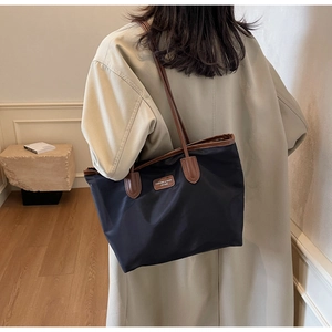 Woman in beige trench coat carrying a large black nylon tote bag with brown handles