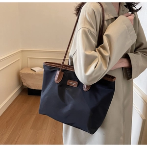 Close-up of black nylon tote bag with leather straps and logo on a model in beige coat