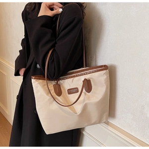 Detailed view of beige nylon tote bag with brown leather trim worn with a black coat