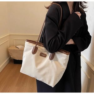 Detail of minimalist tote bag with cream nylon and brown leather strap and logo