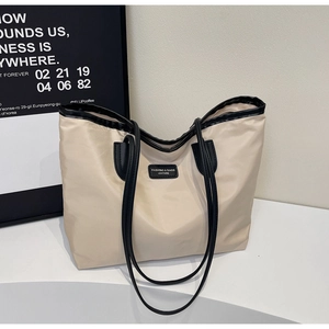 Close-up of beige nylon tote bag with black leather patchwork and minimalist logo plate
