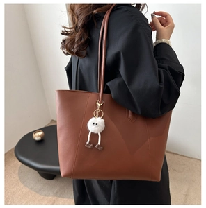 Brown leather tote bag detail with long shoulder straps and white plush monster charm