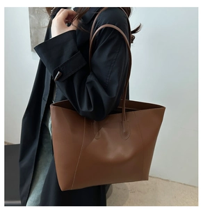 Brown faux leather tote bag with stitch details shown on a trench coat shoulder