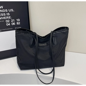 Close-up of black waterproof nylon tote bag with leather logo patch on white surface