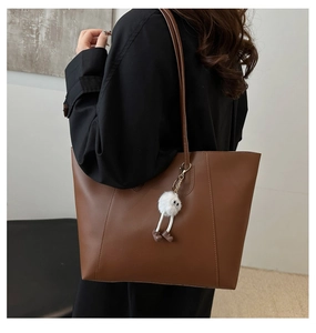 Close-up of vintage brown tote bag with plush monster charm on a female model
