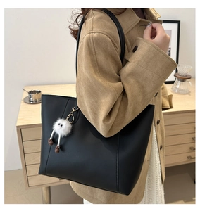 Detail of a black leather tote bag with a white plush monster charm and stitched edges