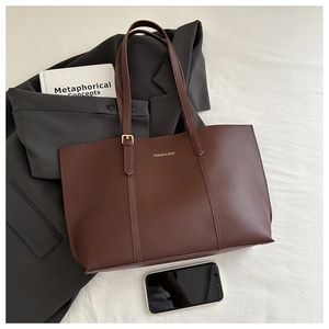 Détail du grand sac cabas marron foncé avec lettrage doré sur un costume gris