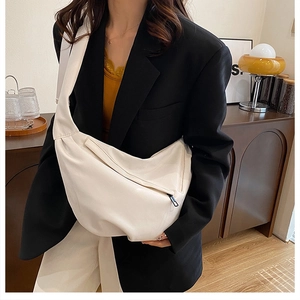 Detail of a beige crescent crossbody bag with zipper pocket worn by a model in a black suit