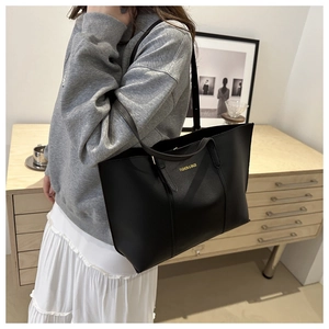 Détail d'un sac cabas noir en similicuir avec logo doré et longue bandoulière chic