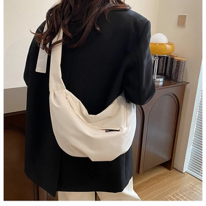 Close-up of minimalist cream half-moon crossbody bag with soft textured fabric and zipper