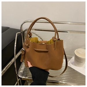 Detail of caramel leather bucket bag featuring knot handles and yellow lining interior