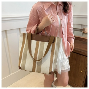 Detail of canvas tote with brown stripes and leather trim held by a model