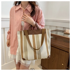 Detail of a large capacity striped canvas tote bag with leather handles shown by model
