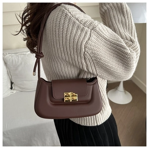 Detail of dark chocolate crossbody bag with golden cross clasp on a beige sweater