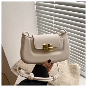 Detailed shot of cream shoulder bag with chocolate-shaped gold buckle and knotted strap
