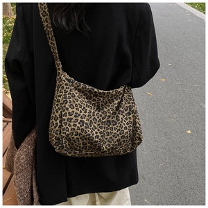 Detail of a large leopard print crossbody hobo bag worn with a black coat in outdoor setting
