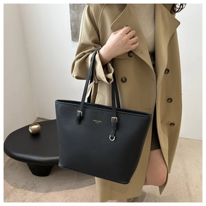 Detail of black leather tote bag with gold logo and adjustable metallic buckle on strap