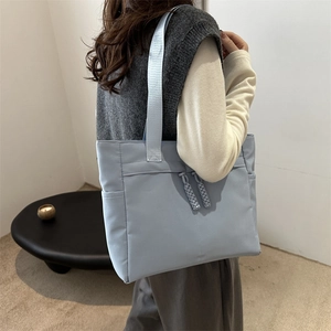 Light blue large capacity tote bag made of glossy nylon fabric shown on a model's shoulder