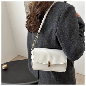 Sac bandoulière blanc en cuir avec boucle dorée et chaîne sur un blazer gris