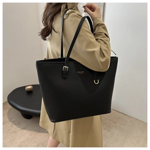 Detail of black leather tote bag with gold hardware and logo on model in stylish trench coat