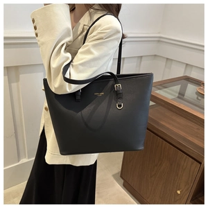 Close-up of black leather tote bag featuring gold brand logo and elegant handle detail