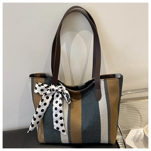 Detailed close-up of striped canvas tote bag with brown leather straps and polka dot ribbon