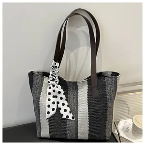 Detail of striped canvas tote bag with leather handles and decorative polka dot scarf