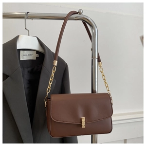 Détail d'un sac bandoulière en cuir marron avec boucle dorée et bandoulière chaîne