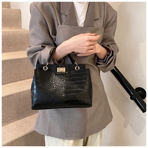 Detail of black faux crocodile skin texture and gold twist-lock on a chic tote bag