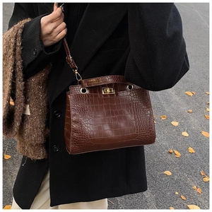 Brown crocodile embossed leather handbag with gold lock shown in an autumn street setting
