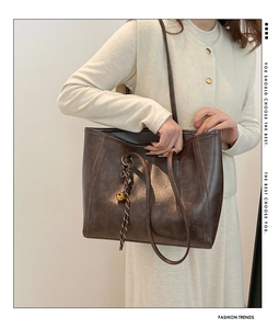 Gros plan du sac cabas marron foncé avec texture cuir mat et détail de breloque tressée