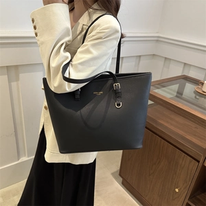 Classic black leather tote bag with gold lettering shown on a model in a cozy interior