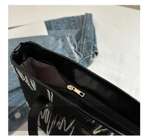 Détail de la fermeture éclair dorée et broderie ondulée sur le sac cabas noir