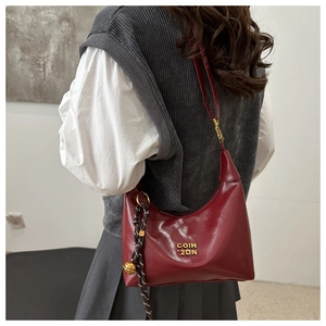 Detail view of burgundy crescent bag with gold metal letters and woven bell pendant