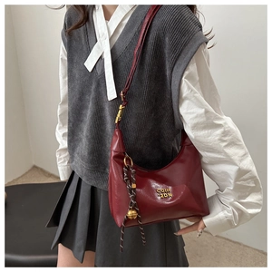 Detail of retro burgundy dumpling bag with golden logo and bell charm on a model
