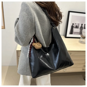 Detail of glossy black leather tote bag with a cute brown teddy bear plush charm