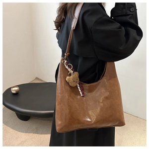 Detail of soft brown tote bag featuring a cute plush bear charm and ribbon accessory